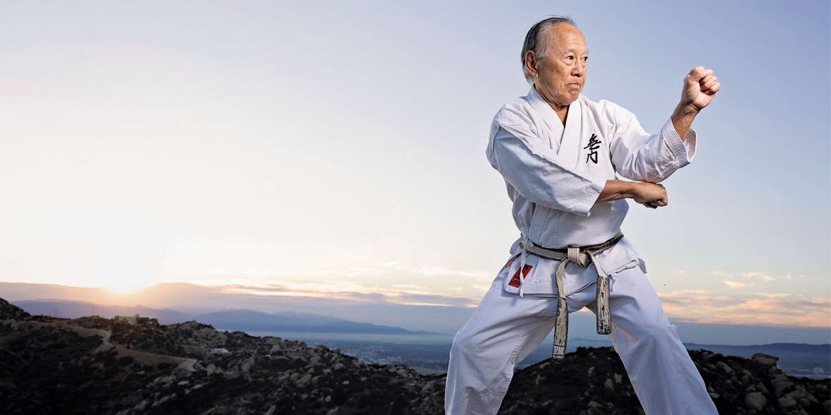 Bruce Kanegai does a karate move with sweeping mountain views behind him.