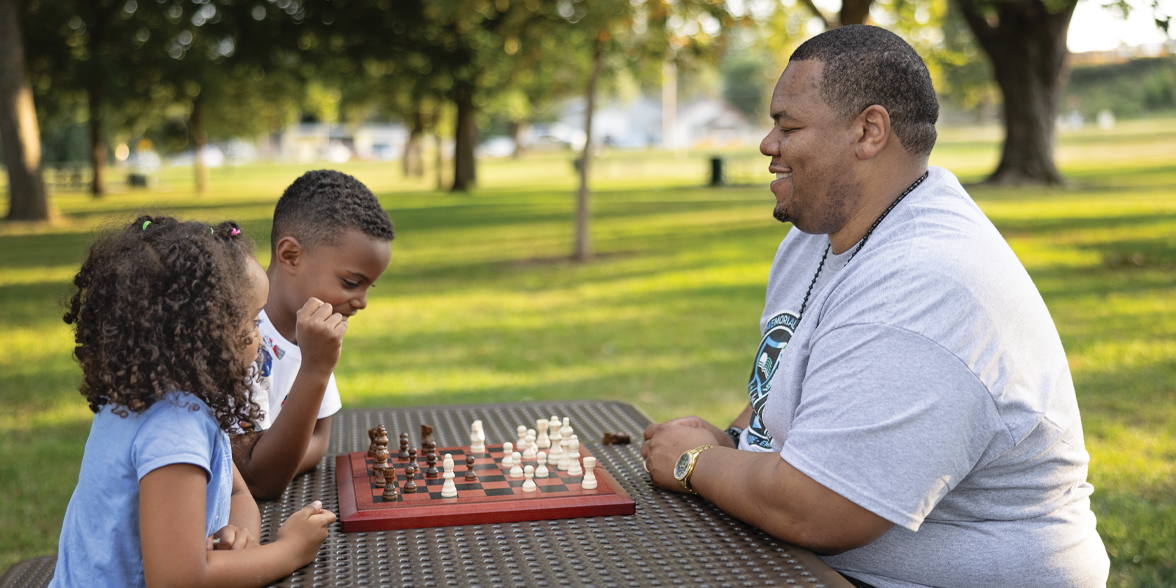 Gibril S. Mansaray juega ajedrez con dos niños en un parque.